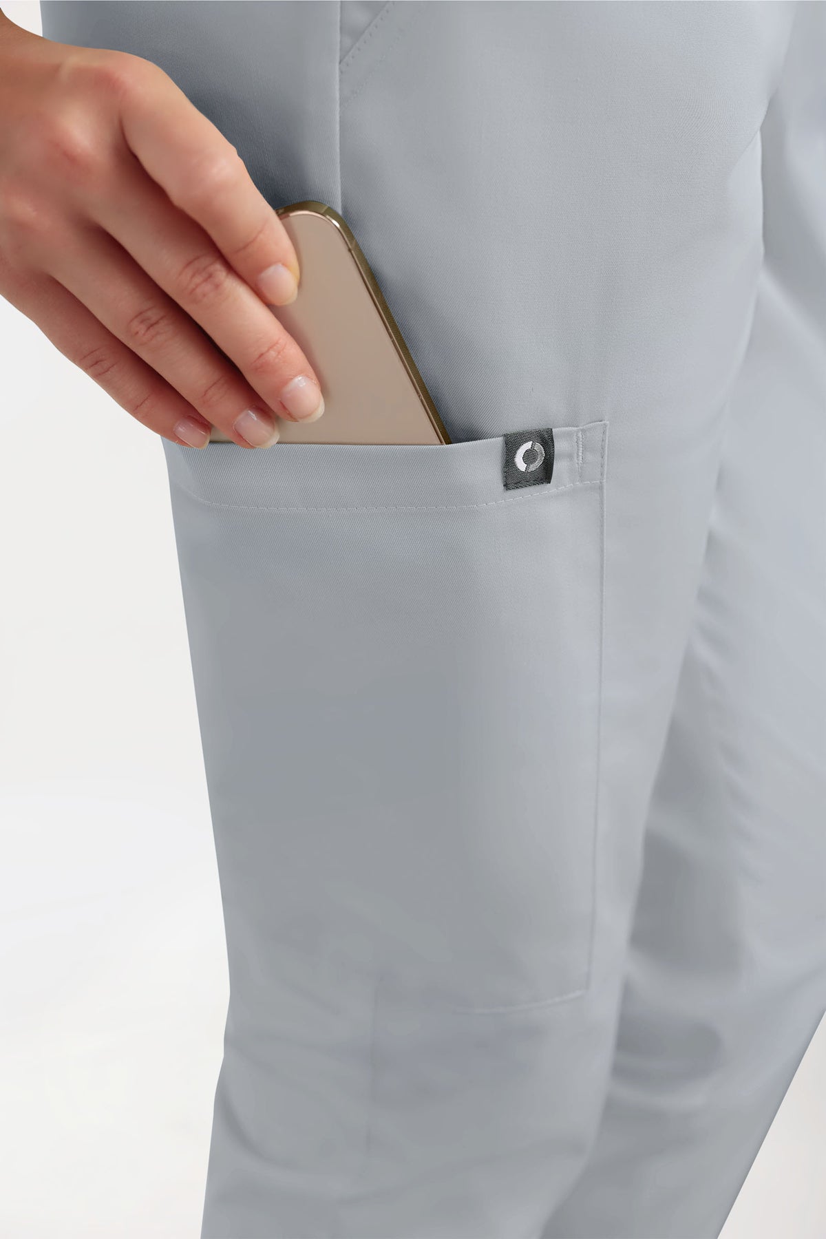 Eine Hand, die ein Smartphone in die Tasche einer hellgrauen GREEN Stretch-Hose für Damen – im Jogginghosen-Stil, Farbe Perlgrau – steckt, die eine lässige, lockere Passform hat.