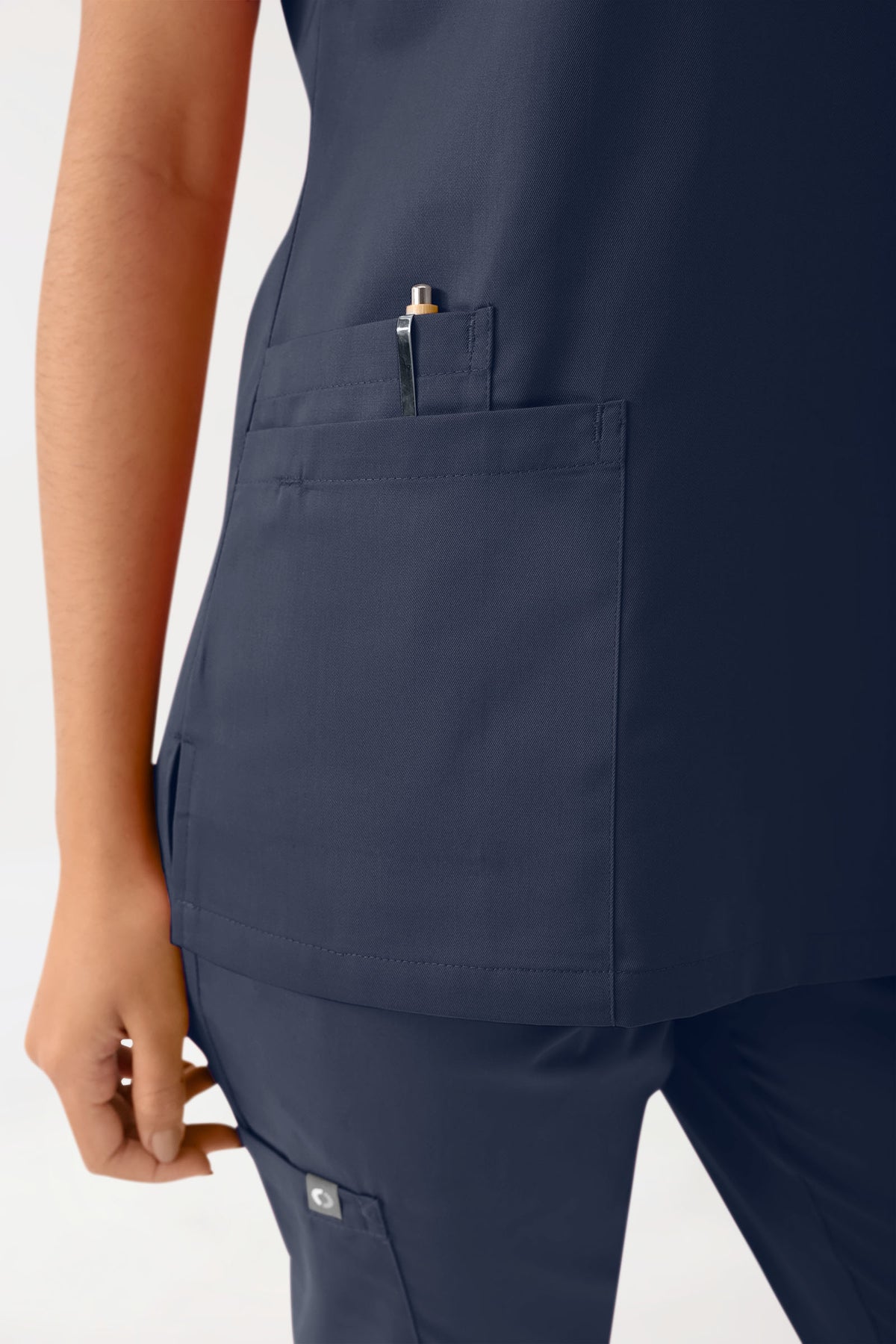 Marineblaues CLINIC DRESS Stretch-Schlupfkleid für Damen – marineblaues OP-Oberteil mit V-Ausschnitt, Brusttasche mit Stifthalter und Armtasche, kombiniert mit einer passenden OP-Hose mit Seitentaschen.