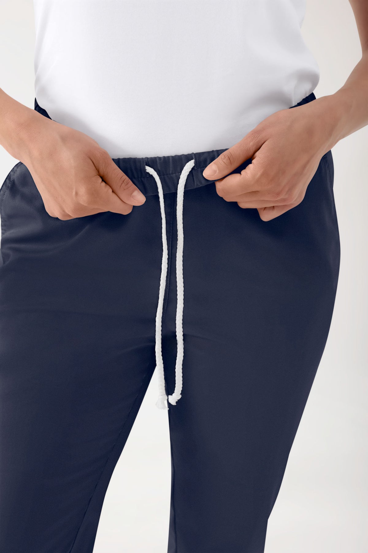 Eine Person, die den weißen Kordelzug an einer Hose der Marke Stretch Hose Unisex – Rundumgummibund in Marineblau mit lockerer Beinpassform und elastischem Bund justiert.