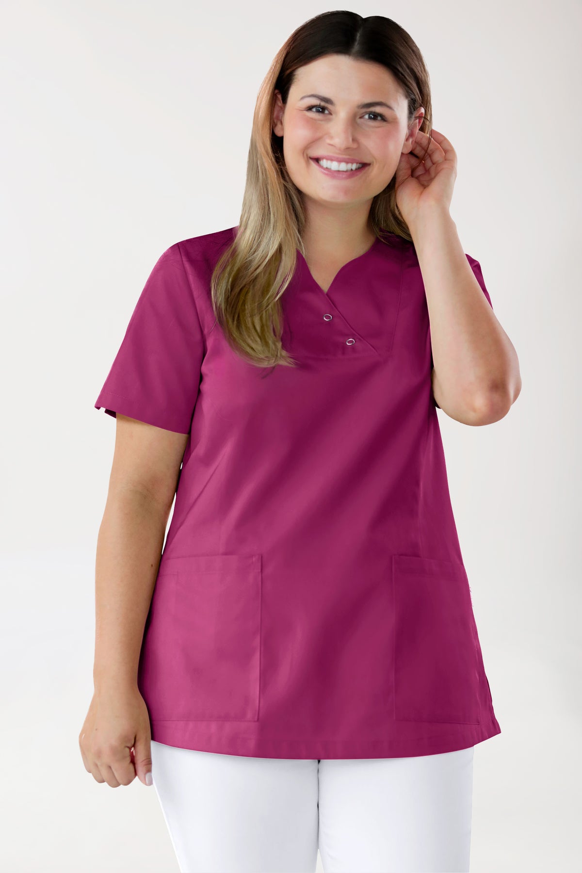 Eine Frau, die ein beerenfarbenes CLINIC DRESS CORE Schlupfkasack Damen Curved Fit – mit Druckknöpfen trägt, ein OP-Oberteil im Wickelstil mit V-Ausschnitt, zwei Druckknöpfen und kurzen Ärmeln.