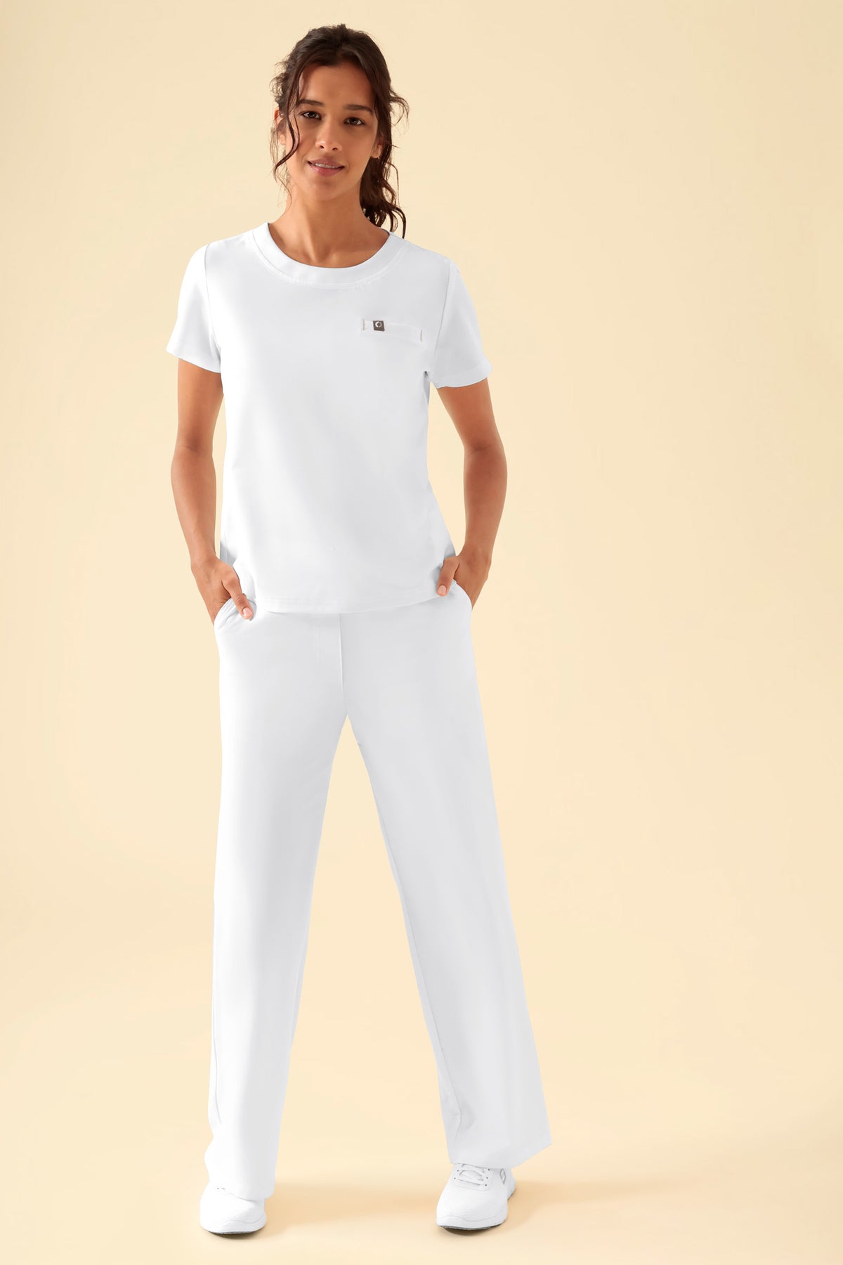 Frau in einem weißen KAERE-Shirt für Damen – Rundhalsausschnitt, weiß, mit Brusttasche und dazu passender weißer Hose.