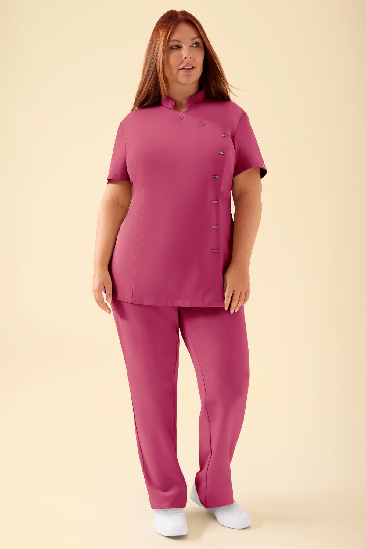 Eine Person trägt einen rosafarbenen KAERE Kasack für Damen mit Stehkragen, asymmetrischem Knopfverschluss und einer dazu passenden Hose., Vorderansicht Das Model ist 173 cm groß und trägt Größe XL