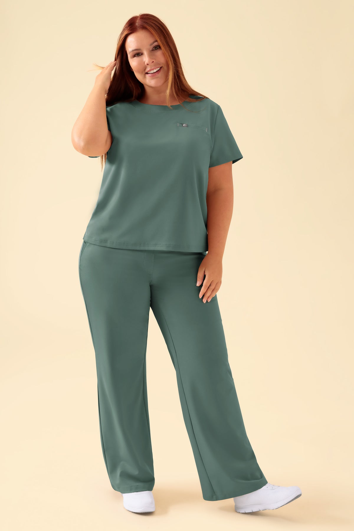 Eine Frau, die ein dunkelgrünes KAERE-Shirt für Damen – Rundhalsausschnitt, dunkelgrün – mit Rundhalsausschnitt und einer Brusttasche trägt, dazu eine passende OP-Hose., Vorderansicht Das Model ist 173 cm groß und trägt Größe XL
