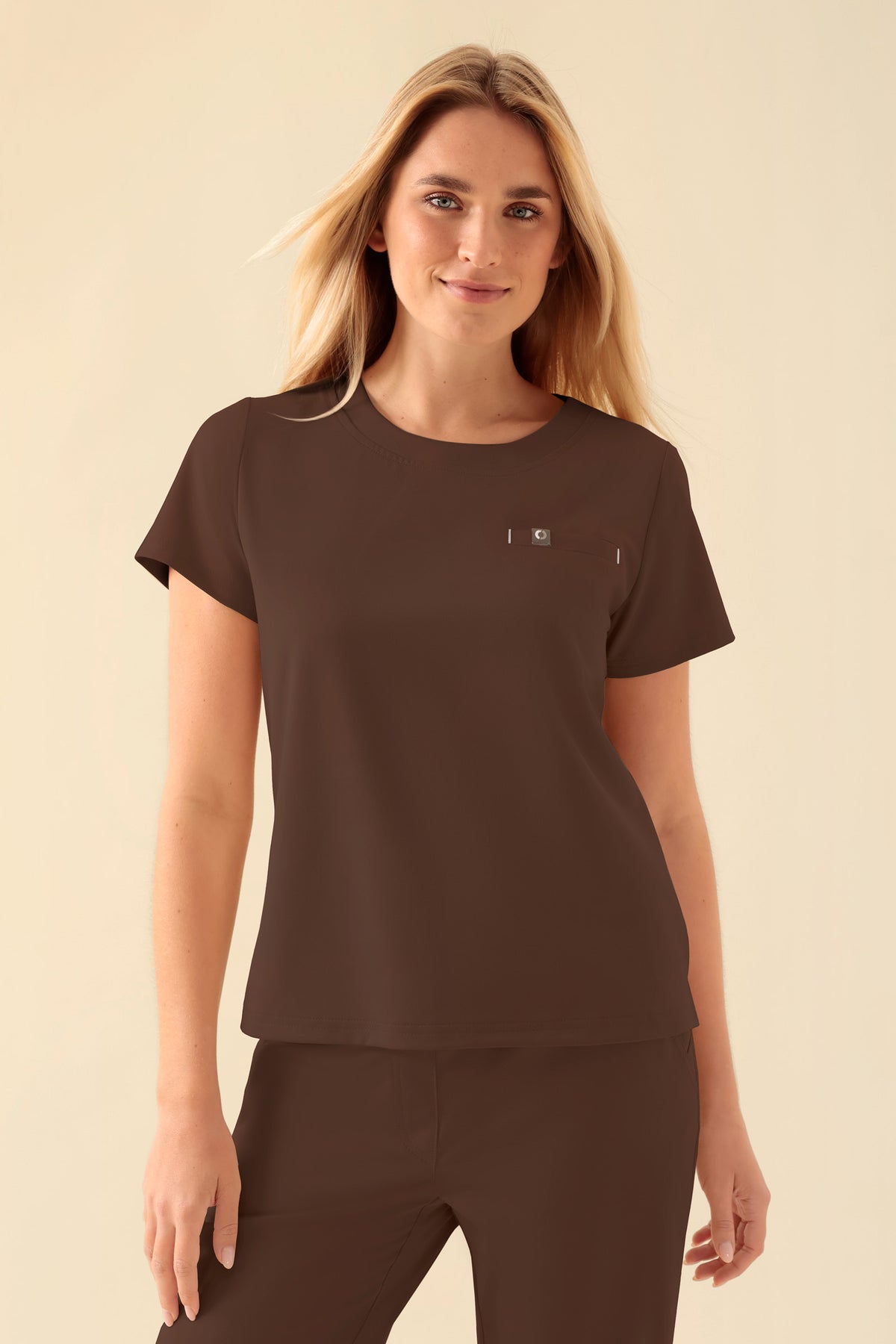 Eine Frau, die ein braunes KAERE-Shirt für Damen – Coffee – mit Rundhalsausschnitt, Seitenschlitzen und einer kleinen Brusttasche trägt.