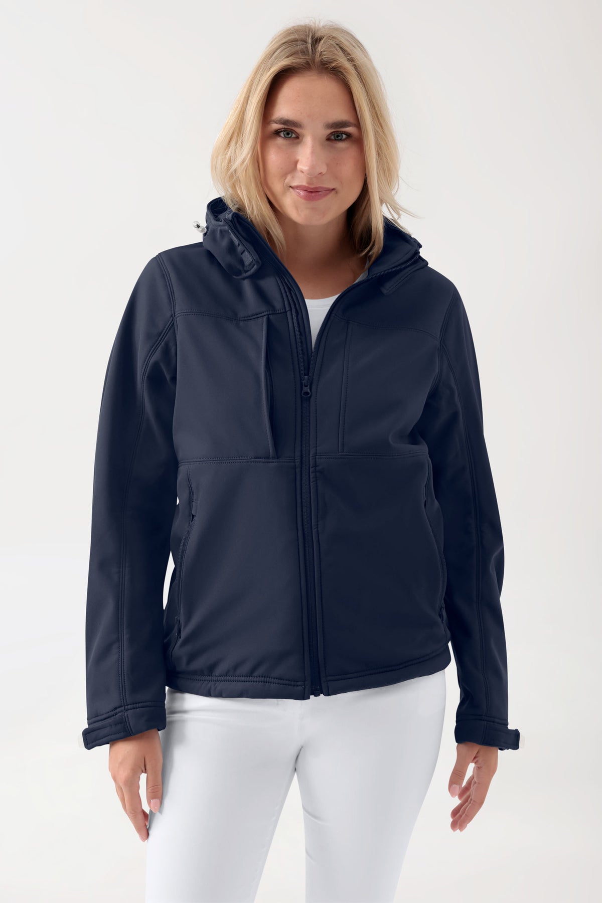 Eine Person, die eine atmungsaktive, wasserabweisende, marineblaue CLINIC DRESS Softshell-Jacke (Unisex) mit abnehmbarer Kapuze trägt.