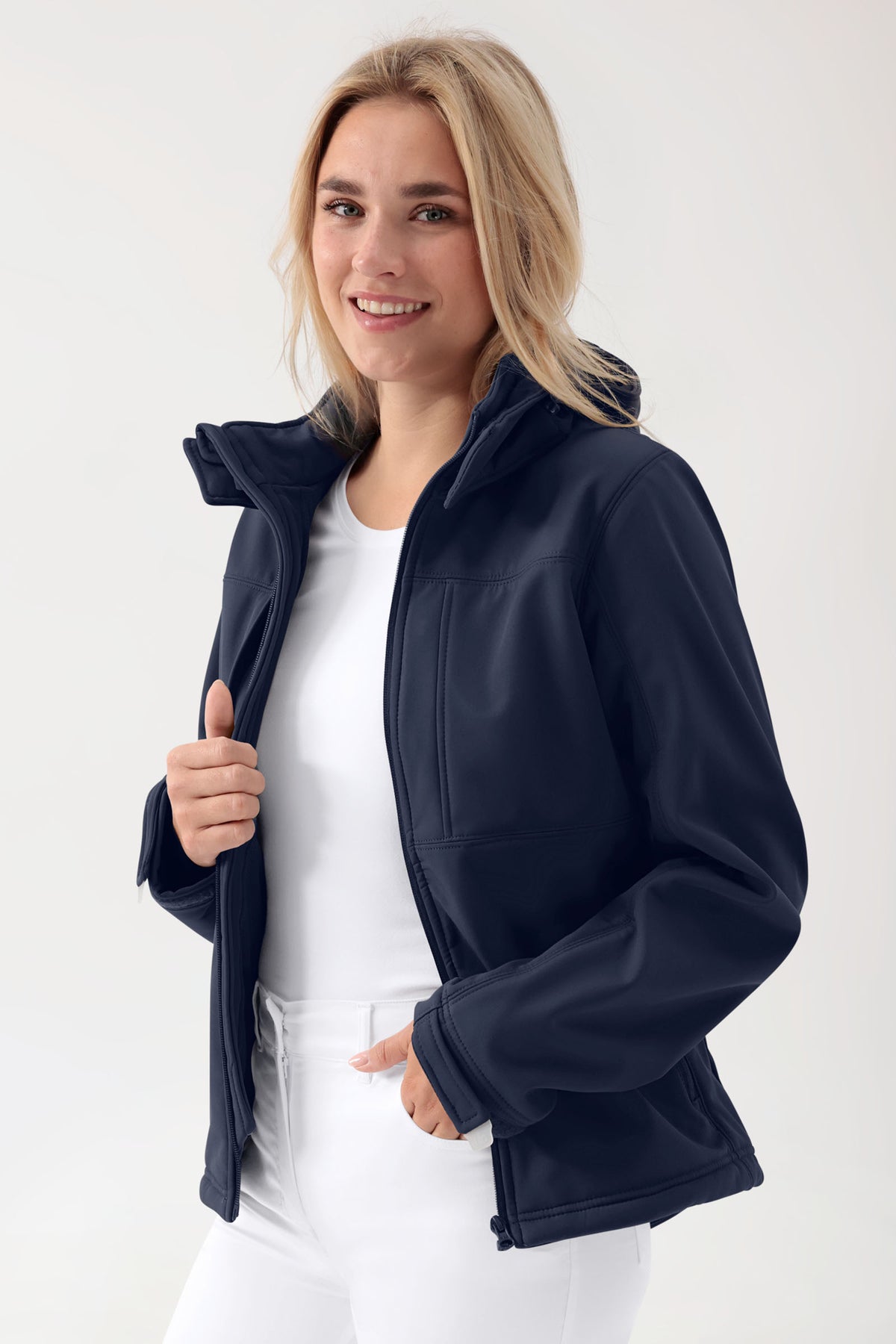 Frau, die eine marineblaue Softshell-Jacke (Unisex) – mit abnehmbarer Kapuze in Marineblau – über einem weißen Hemd trägt.